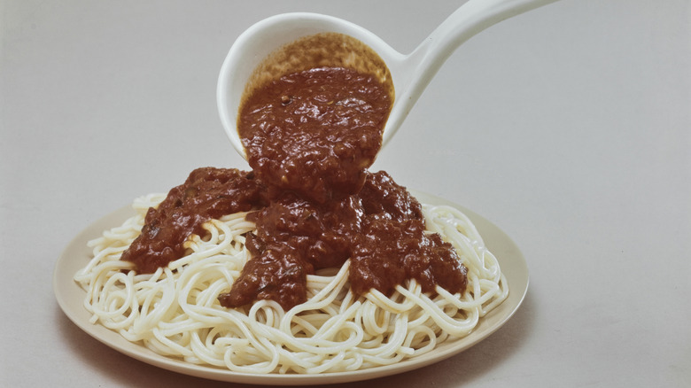 White ladle pouring spaghetti sauce onto spaghetti on white plate with white background