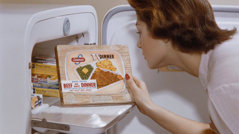 Woman looks at TV dinner as she removes it from freezer