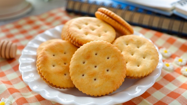 a white plate of Ritz crackers on a gingham cloth next to a notebook and honey dipper