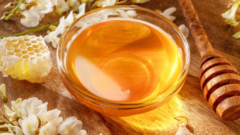 a small bowl of honey next to a honey dipper, honeycomb, and flowers on a wooden background