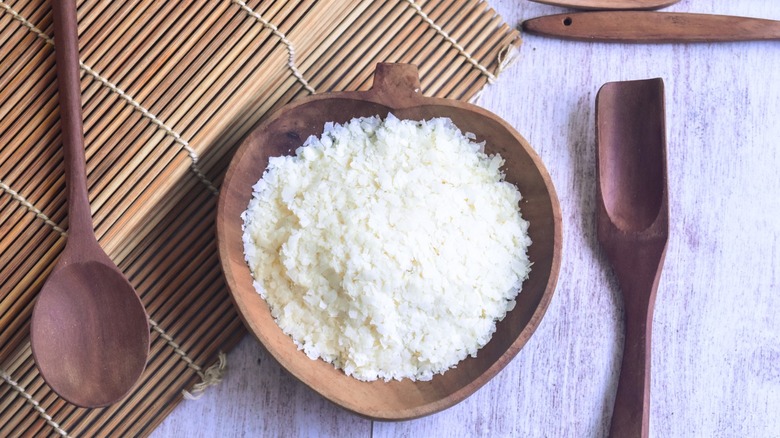 a wooden bowl of potato flakes next to wooden spoons and mat