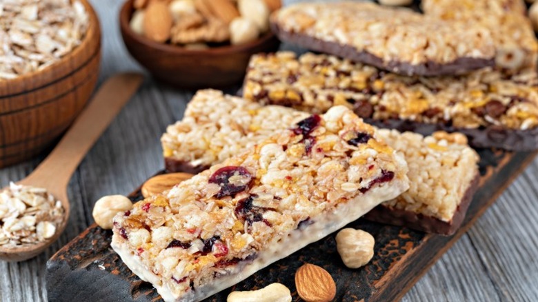 granola bars dipped in chocolate with dried fruit next to bowls of oats and nuts