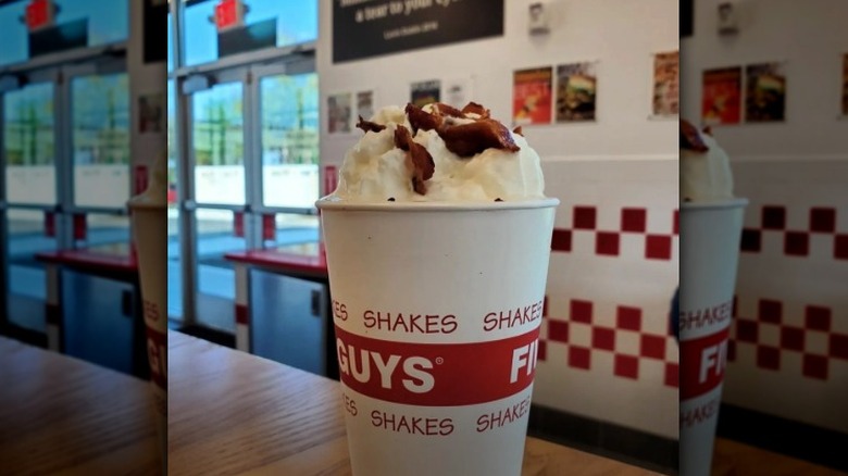 A Five Guys bacon milkshake with whipped cream on a table inside the fast food restaurant