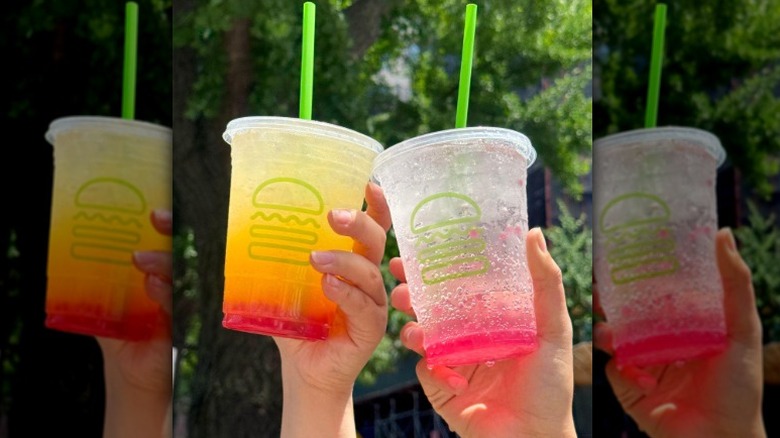 two hands holding a yellow and clear drink from Shake Shack with raspberry popping boba