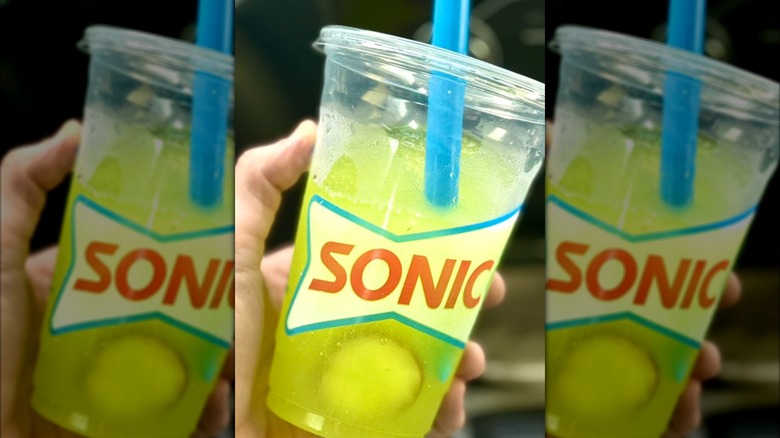 hand holds Sonic Picklerita slush in plastic cup with big straw and pickle slices inside