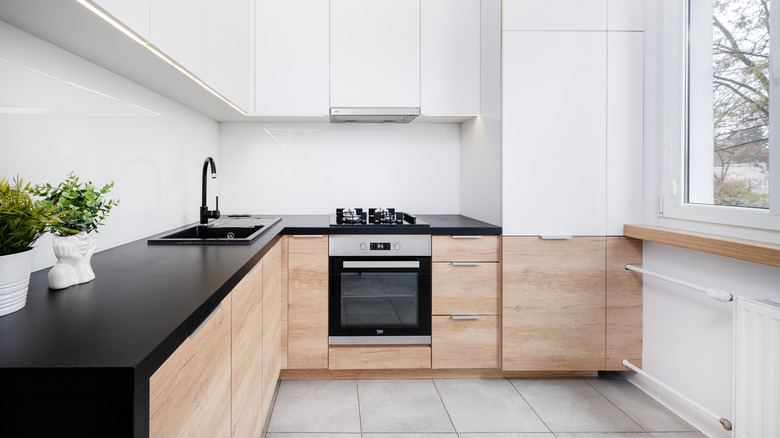 A small kitchen with white walls, wooden cabinets, and a black countertop and sink