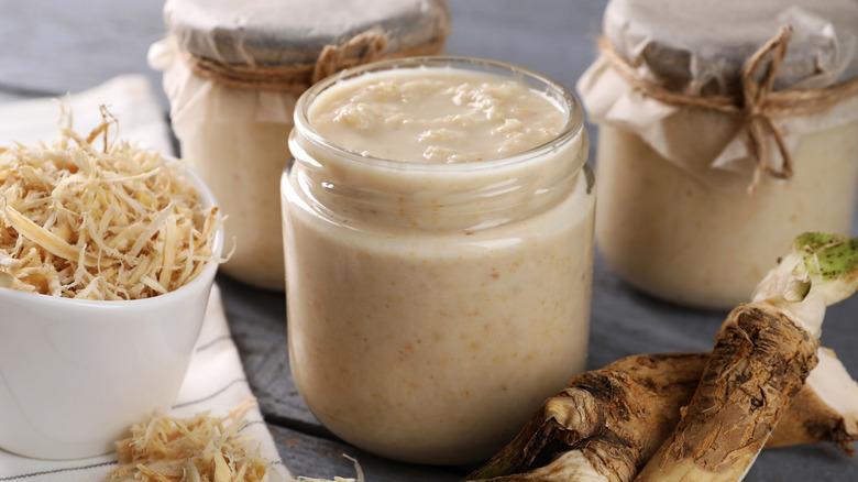 Horseradish sauce in a jar surrounded by grated horseradish