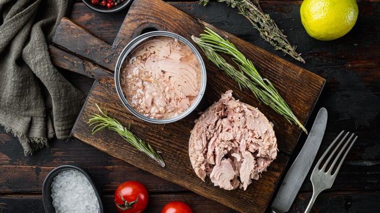Can of tuna and heap of tuna on wooden board