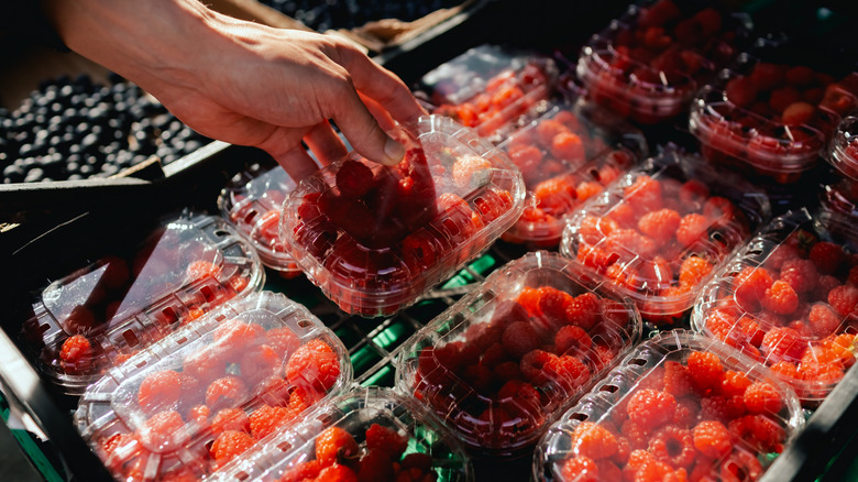 a hand picking up a clear plastic container of pale colored raspberries from a market shelf