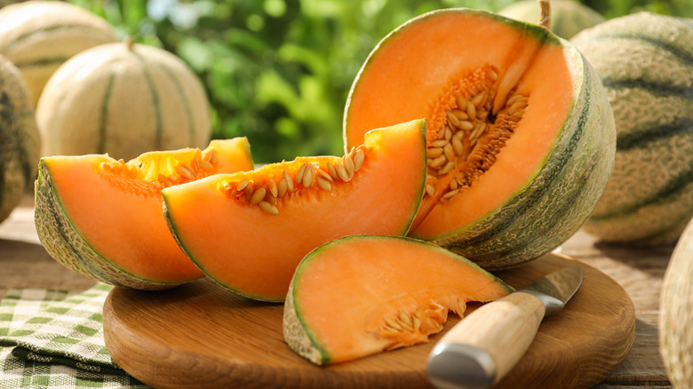 Two slices of ripe cantaloupe and whole melons