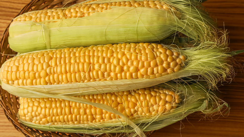 a close up of raw corn on the cob with bits of husk and cornsilk