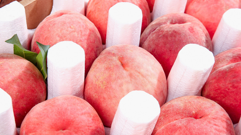 Fresh ripe peaches with protective white foam sleeves arranged in wooden crate, ready for market sale or shipping