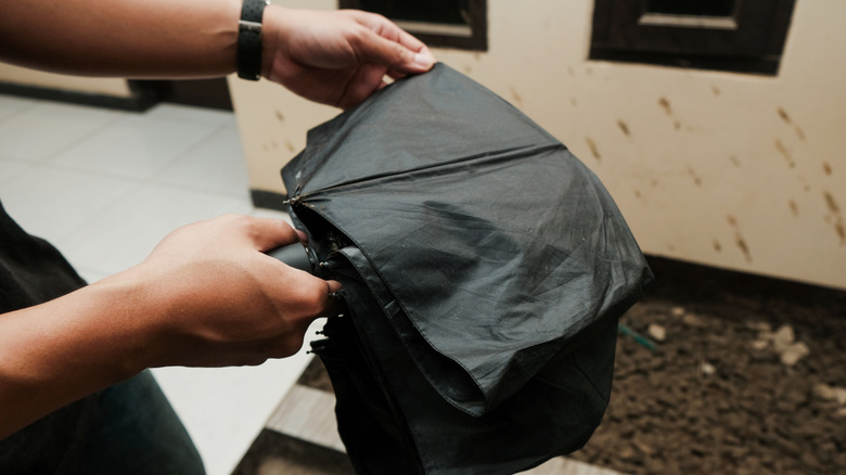 Close-up of a man's hands closing an umbrella indoors