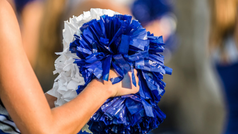 A close-up of a cheerleader holding a blue and white pom-pom