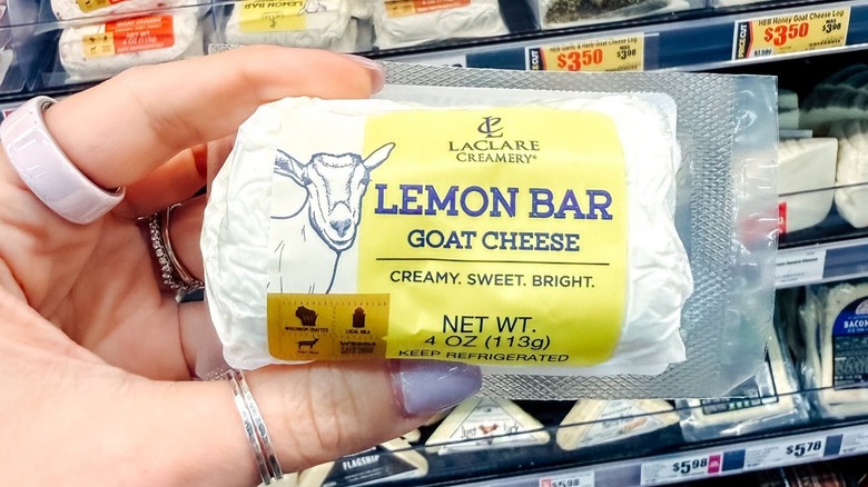 Someone holding a log of lemon goat cheese inside a grocery store.