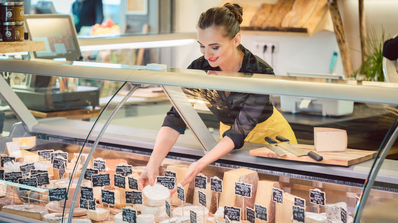 A woman arranging cheese inside a glass case.