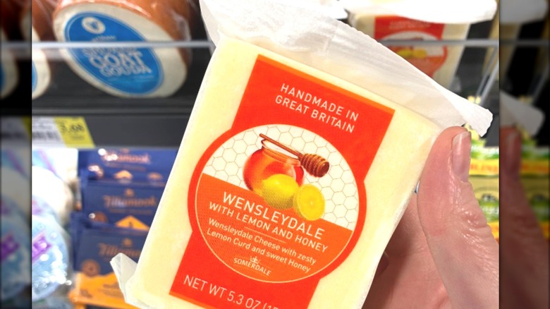 Someone holding British Wensleydale cheese in a cheese aisle.