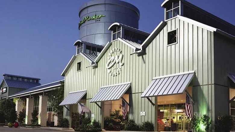 A Central Market in a green, barn-like structure with a a large silo displaying the store name in green letters