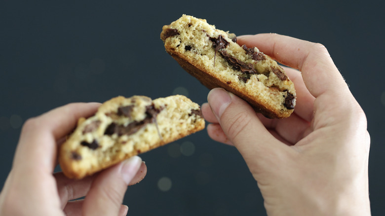 hands holding thick chocolate chip cookie snapped in half