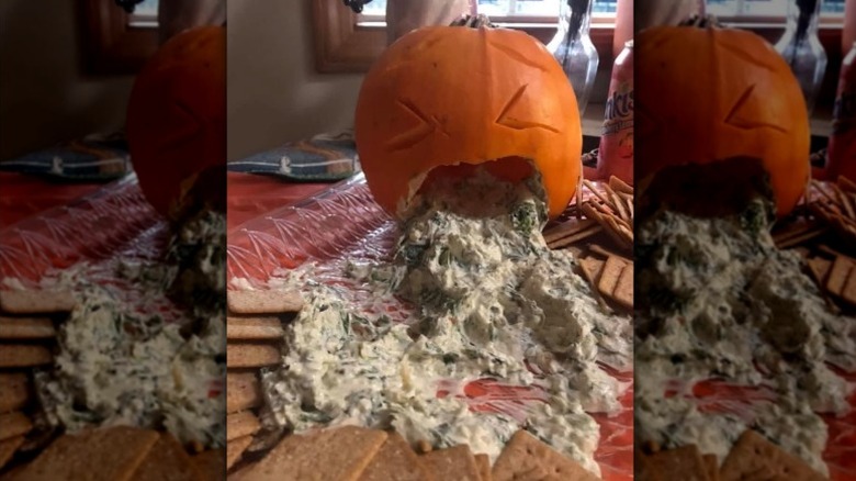 jack o'lantern with spinach dip coming out of its mouth opening on a table with crackers