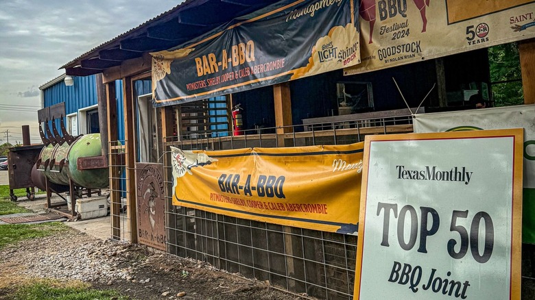 The exterior of Bar-A-BBQ restaurant with signs and the smokers to the side