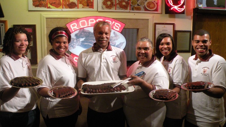 Roper's Ribs staff standing in front of the sign in the entryway holding platters of ribs.