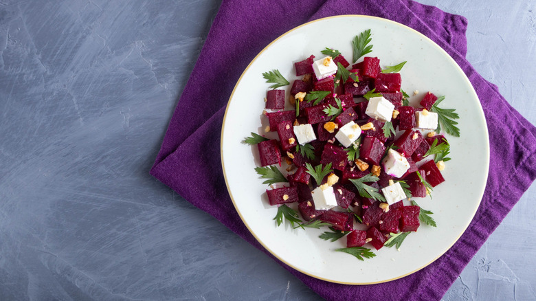 Beetroot, feta, and walnut salad on a white plate on a purple cloth