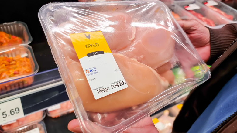 Customer holding packaged container of chicken breasts at Aldi