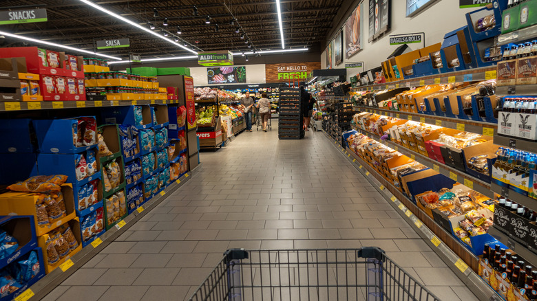 Shopping cart before an aisle of snacks, beverages, and produce at Aldi