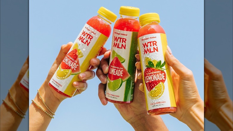 Three hands holding up three bottles of watermelon water