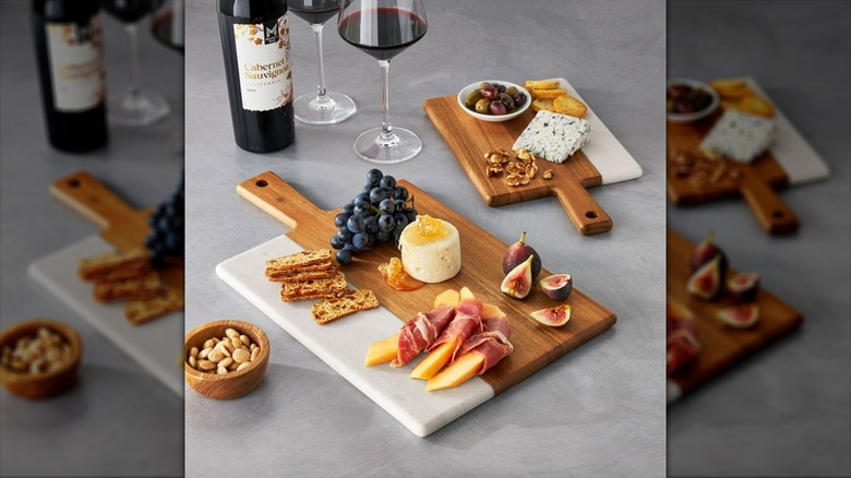 Member's Mark Marble & Acacia Wood Charcuterie Boards with grapes, crackers, wine, and other foods on gray countertop