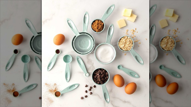 Nordic Ware Sea Glass Blue Measuring Cups and Measuring Spoons Set on counter with shelled brown eggs and a variety of ingredients scattered around