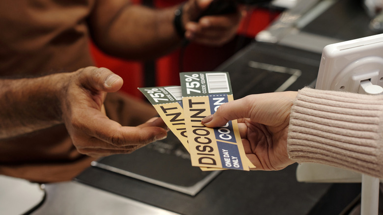 Person handing a cashier some discount coupons