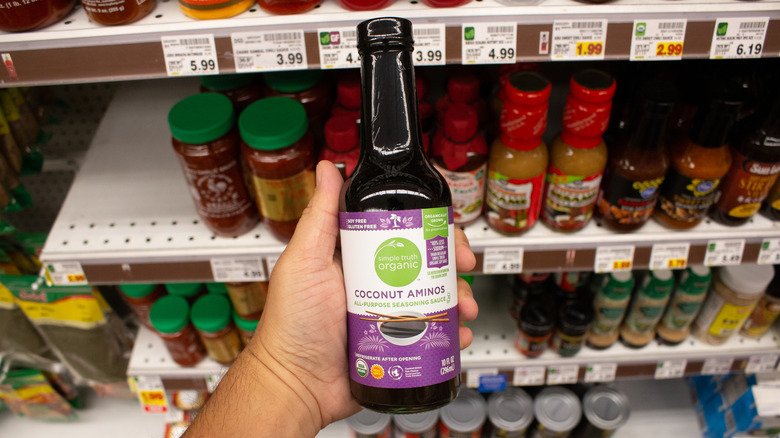 Hand holding simple truth coconut aminos from Kroger