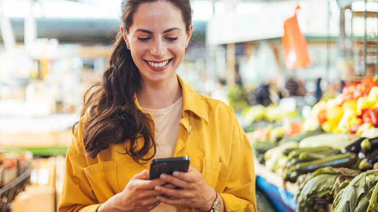 Woman in grocery store smiling at smartphone