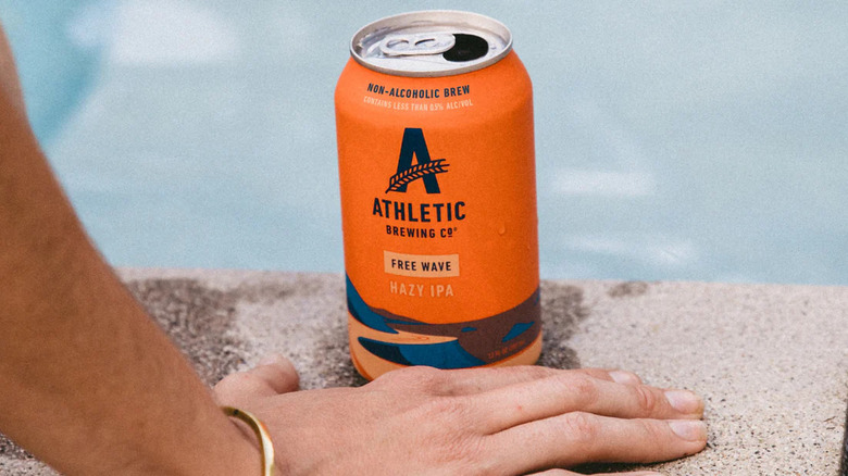 A hand in front of an Athletic Brewing Free Wave, poolside