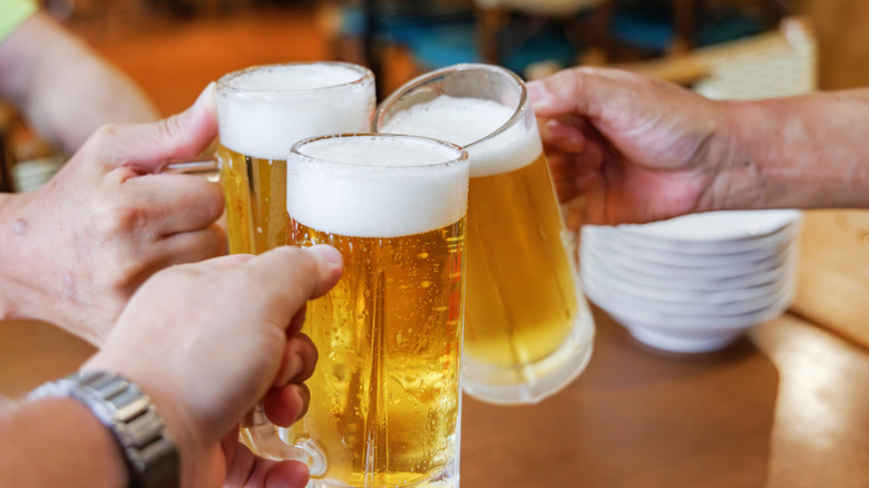 Hands holding and clinking three mugs of cold beer at a restaurant