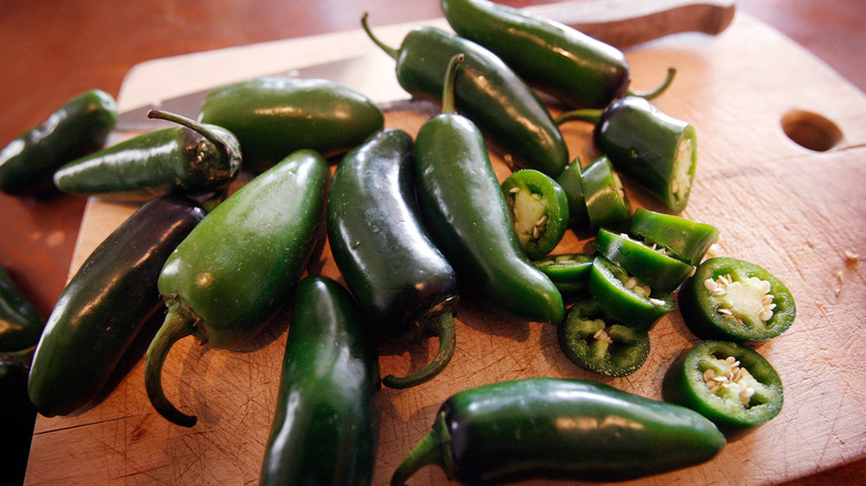 whole and sliced jalapeños on a wooden board