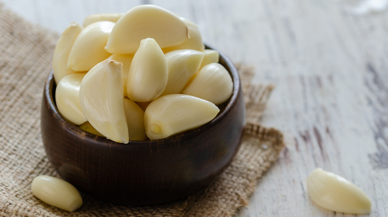 Peeled garlic cloves in a small brown bowl sitting on a piece of burlap