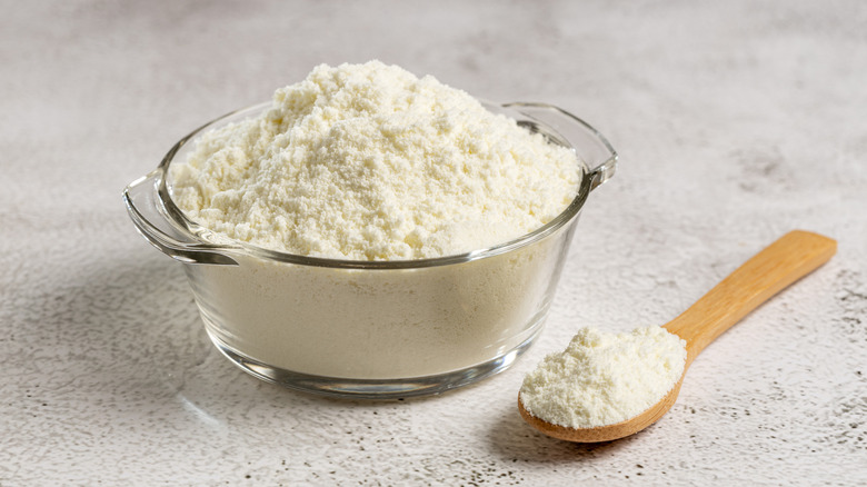 powdered milk in a clear bowl and a wooden spoon
