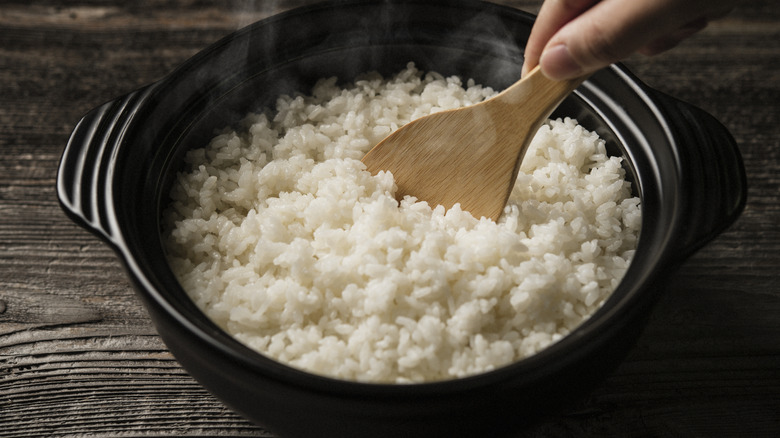 Hand of person stirring white rice in black ceramic bowl