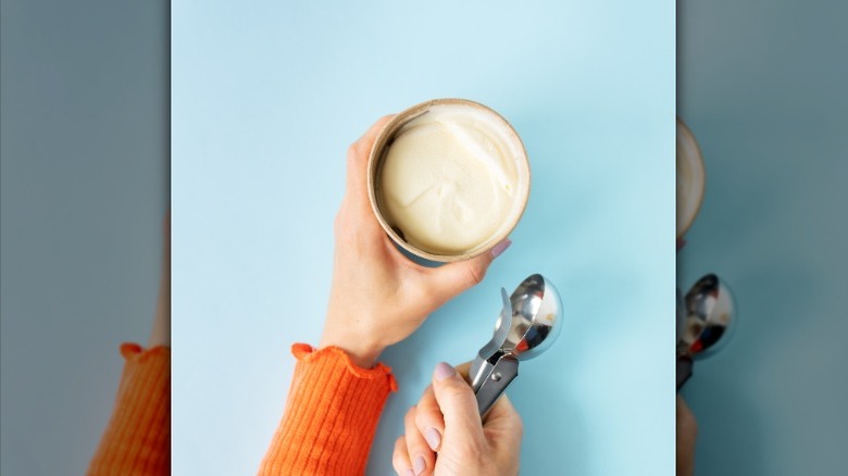 Person holding cup of ice cream and scoop