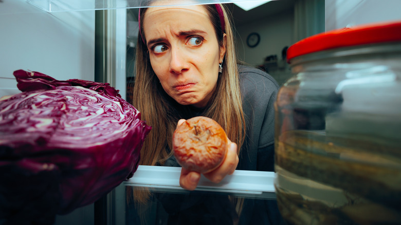 Woman taking spoiled piece of fruit out of refrigerator