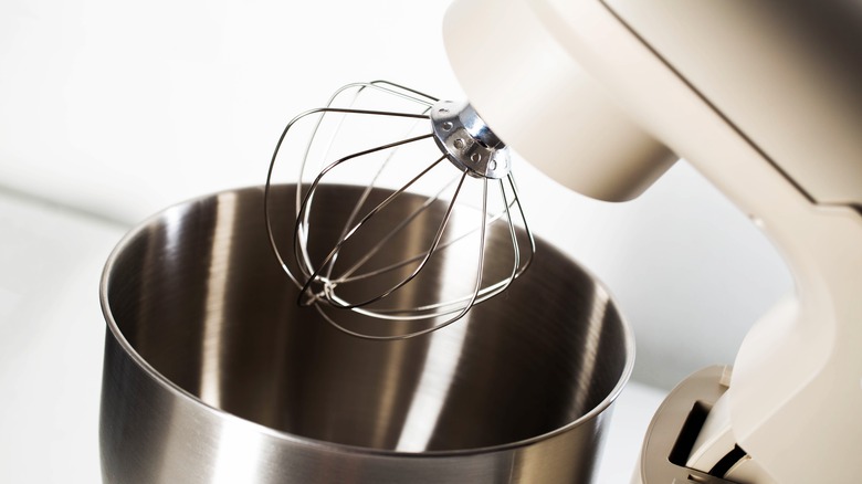 Close-up view of modern stand mixer with wire whisk attachment positioned inside empty, shiny stainless steel mixing bowl