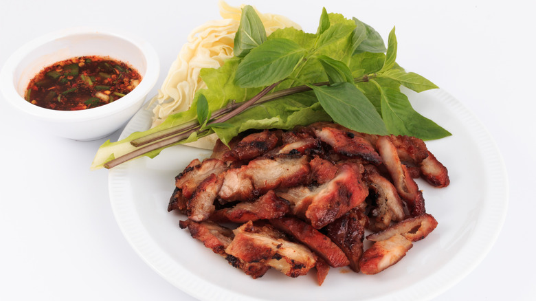 Roasted pork on a white plate with a bowl of spicy dip