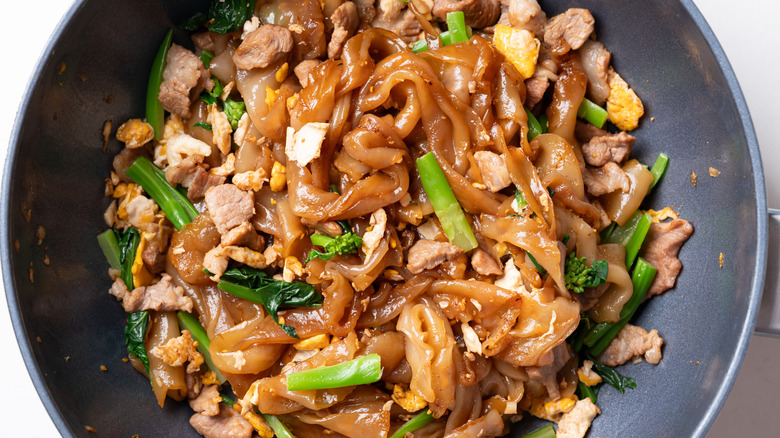A wok filled with stir fried Thai noodles and meat