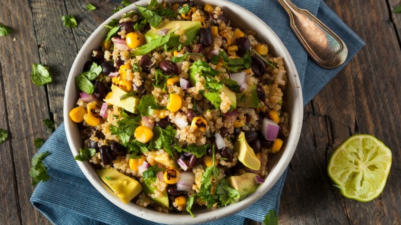 Grain bowl with quinoa, black beans, corn, onions, and cilantro sits on a blue cloth on a wooden surface