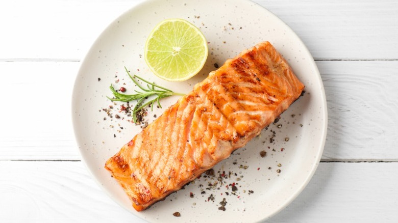A salmon fillet on a white plate with lemon and herb garnish