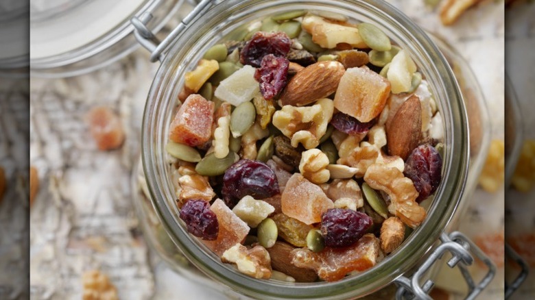 a glass mason jar filled with trail mix with walnuts, almonds, pumpkin seeds, cranberries, and dried fruit