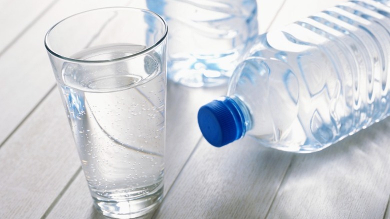 a glass of water and two water bottles on a white painted wooden tabletop